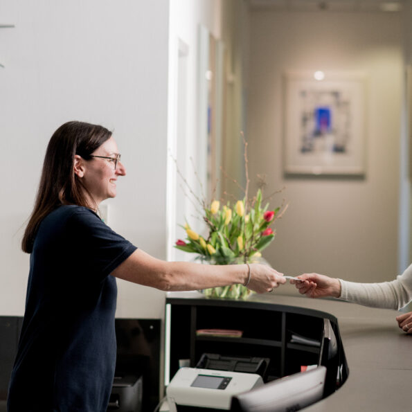Angestellte übergibt Patientin an der Rezeption eine Visitenkarte